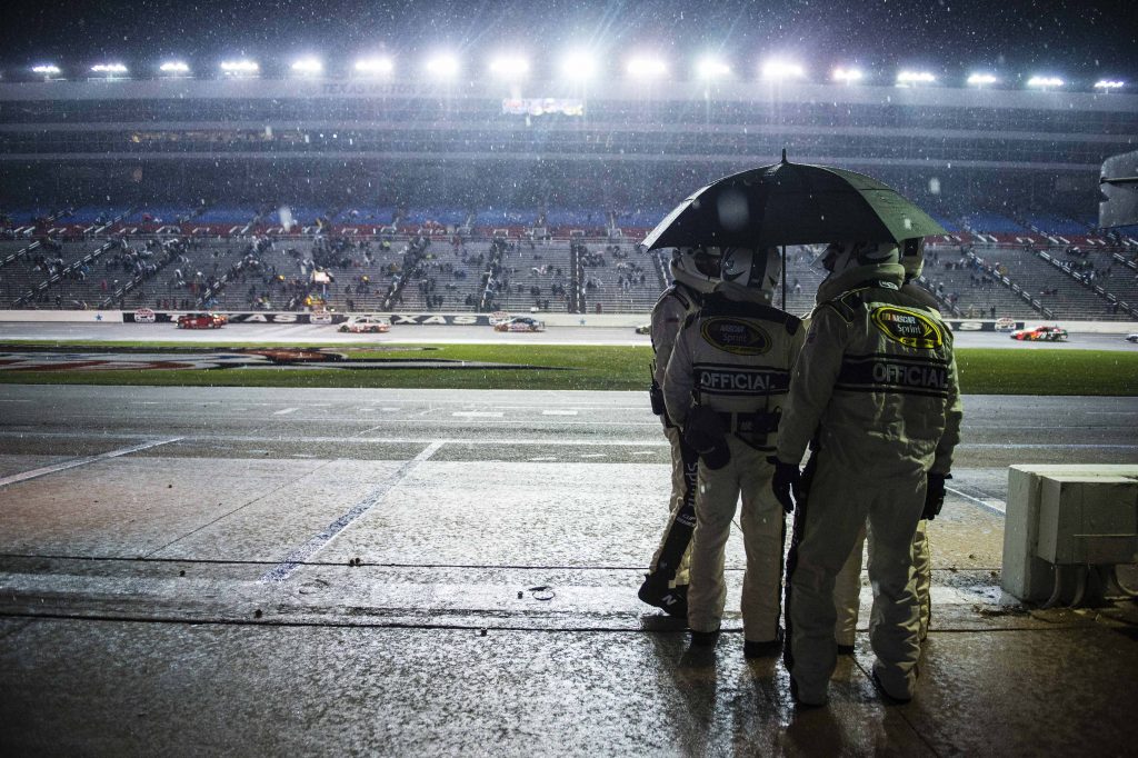 Nov 6, 2016; Fort Worth, TX, USA; NASCAR officials huddle under an umbrella as Sprint Cup Series driver Carl Edwards (19) and driver Joey Logano (22) drive by in the rain during the AAA Texas 500 at Texas Motor Speedway. Mandatory Credit: Jerome Miron-USA TODAY Sports