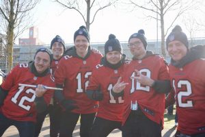 A group of Tom Brady fans smile as they prepare to perform their drum line cadences. The group plays as a drum line to garner spirit for other fans prior to games.