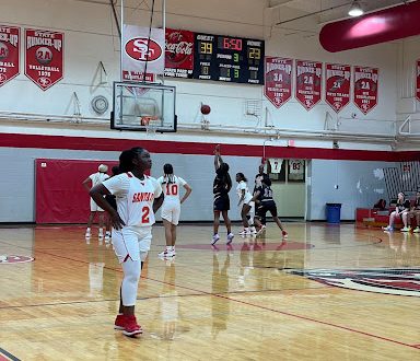 A Santa Fe basketball player looks at the scoreboard, unhappy, as a Columbia player makes a free throw behind her.