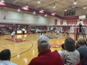 Two Bishop Moore players attempt to block the ball as it crosses over the net