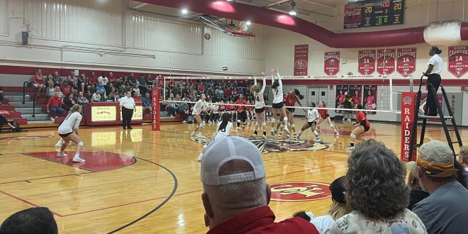 Two Bishop Moore players attempt to block the ball as it crosses over the net